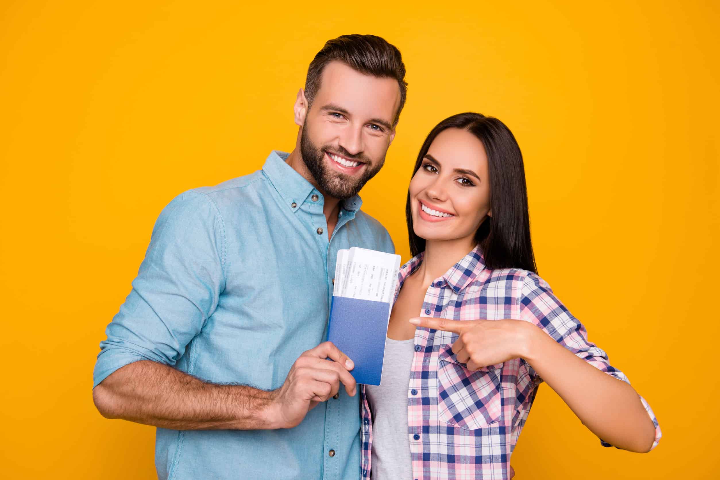 joyful glad couple holding passport with flying tickets in hands